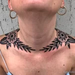 Фото тату: Две симметричные цветочные татуировки украшают шею и ключицы девушки. Рисунок татуировки выполнен в черном цвете с использованием тонких линий и точечной техники.