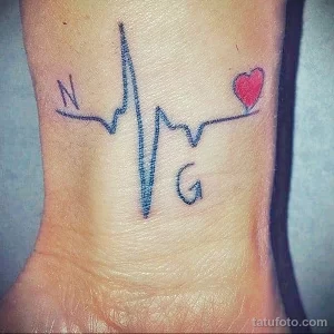 Фото тату на запястье, изображающее линию пульса с инициалами 'N' и 'G' и сердечком. Черно-белый рисунок, персонализированный дизайн.
