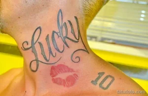 Фото тату надписи 'Lucky' с отпечатком губ и цифрой 10 на шее. Черно-серые оттенки, романтический стиль, уникальный дизайн. Подходит для тех, кто хочет увековечить важную дату или человека.