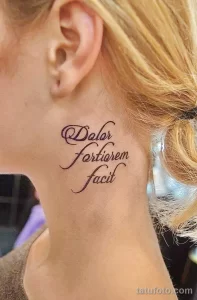 Фото тату латинской фразы 'Dolor Fortior Fecit' на шее. Изящный шрифт, фиолетовые оттенки, женственный стиль. Подходит для тех, кто ценит мудрость и силу духа.