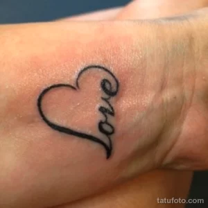 Маленькая черно-белая татуировка на запястье с надписью 'Love', стилизованной под форму сердца. Простой и элегантный дизайн.