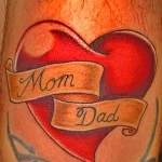 Фото татуировки сердца с надписями 'Mom' и 'Dad' на руке. Красно-коричневые оттенки, мягкие переходы, реалистичный стиль.