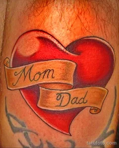 Фото татуировки сердца с надписями 'Mom' и 'Dad' на руке. Красно-коричневые оттенки, мягкие переходы, реалистичный стиль.