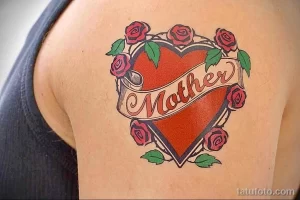 Фото татуировки сердца с надписью 'Mother' и розами в стиле олд скул на плече. Яркие цвета, традиционный дизайн, четкие контуры.
