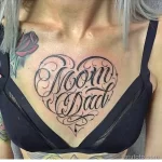 Фото татуировки в виде сердца с надписями 'Mom' и 'Dad' на груди. Черно-белый рисунок, каллиграфический шрифт, элегантный дизайн.