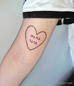 Фото минималистичной татуировки в виде сердца с надписью 'MAMA TATA' на руке. Тонкие линии, простой дизайн, нежный стиль.