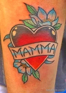 Фото тату сердца с надписью 'MAMMA' в стиле олд скул на предплечье. Яркие цвета, четкие контуры, традиционный дизайн.