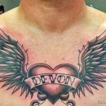 Фото тату: сердце с расправленными крыльями и именем "Devon" на груди. Классический рисунок татуировки, выполненный в серо-черных тонах.