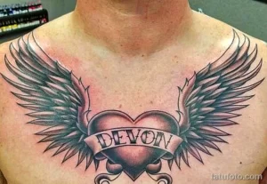 Фото тату: сердце с расправленными крыльями и именем "Devon" на груди. Классический рисунок татуировки, выполненный в серо-черных тонах.