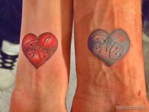 Фото парных тату на предплечьях: красное и синее сердца с инициалами 'F' и 'K' внутри. Романтичный и символичный рисунок татуировки.