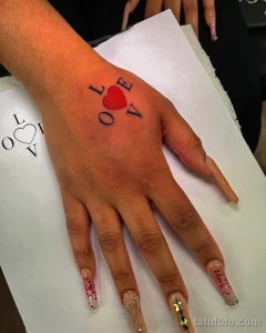 Фото минималистичного тату надписи LOVE, где буква O заменена на сердце. Рисунок татуировки выполнен в красном цвете.