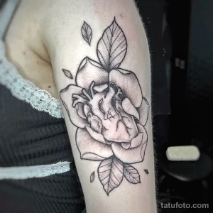 Фото тату: реалистичное изображение сердца, расположенного внутри цветка, выполнено в технике графики и дотворк на руке.