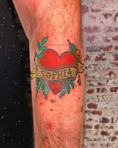 Фото тату на руке: сердце в стиле old school с надписью "Sophia" на ленте. Яркий и красочный рисунок татуировки для девушек.