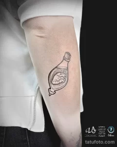 Фото тату на предплечье: реалистичное изображение сердца, заключенного в стеклянную бутылку. Детализированный рисунок татуировки в черно-серых тонах, символизирующий уязвимость и сохранение чувств.