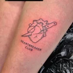 Фото тату сердца, пронзенного ножом, с надписью 'Heartbreaker Club'. Черно-белый рисунок, минимализм, символизм разбитой любви.
