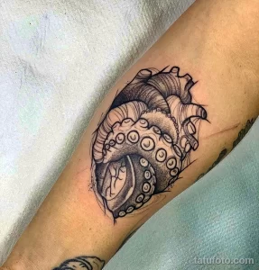 Фото татуировки на руке в стиле blackwork: сердце, из которого вырывается осьминог. Детализированный черно-белый рисунок.