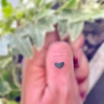 Очень маленькая татуировка в виде сердца, выполненная тонкими линиями, расположена на фаланге пальца.