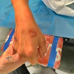 Фото тату небольшого красного сердца, нарисованного тонкой линией на руке, в минималистичном стиле.