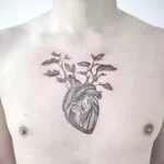 Фото татуировки сердца, из которого растут ветви с листьями, на мужской груди. Черно-белый рисунок с реалистичным изображением сердца и растений.