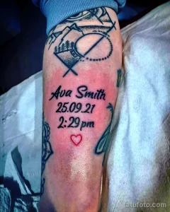 Фото тату на руке: имя 'Ava Smith', дата рождения '25.09.21' и время '2:29pm', украшенное сердцем и геометрическими фигурами.