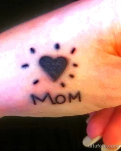 Фото тату сердца и отпечатка лапы с надписью "Mom", выполненного в простом стиле, на пальце. Нежный и трогательный рисунок татуировки.