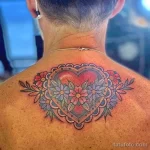 Фото тату сердца, окруженного красочными цветами и декоративной рамкой, на спине. Детализированный рисунок татуировки выполнен в ярких и насыщенных цветах.