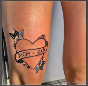 Фото тату на ноге: сердце с надписью "MOM & DAD", украшенное небольшими цветочными элементами. Черно-белый рисунок, символизирующий любовь к родителям.