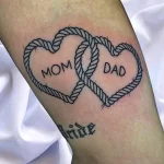 Фото тату на предплечье: два сердца, переплетенные веревкой, с надписями 'MOM' и 'DAD'. Символ родительской любви и связи.