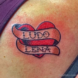 Фото тату на плече: красное сердце с надписями 'Ludo' и 'Lena'. Простая и трогательная татуировка с именами.
