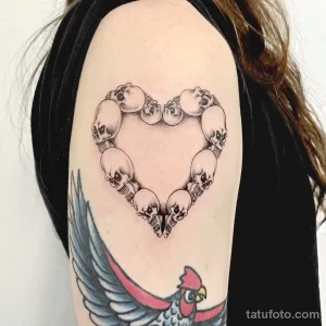 Фото тату на плече: сердце, составленное из черепов, выполненное в технике blackwork. Детализированный рисунок татуировки с четкими контурами.