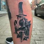 Фото тату: черно-белая татуировка в стиле blackwork на ноге. Изображено сердце, пронзенное кинжалом, с использованием плотных черных заливок.