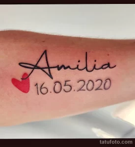 Фото тату: надпись "Amilia" с датой рождения "16.05.2020" и маленьким сердечком на руке. Минималистичный рисунок татуировки.
