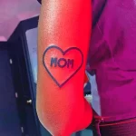 Фото тату небольшого сердца с надписью 'MOM' на руке. Простой и лаконичный дизайн, идеальный для выражения любви к матери.