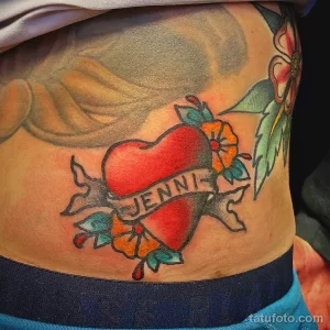 Фото тату сердца с именем "JENNI" на ленте. Яркий, цветной рисунок в стиле олд скул, с использованием традиционных мотивов и цветов.