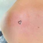 Фото тату: крошечное черное сердце, нанесенное на грудь. Простой и элегантный рисунок татуировки в стиле минимализм.