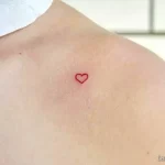 Фото минималистичной татуировки: крошечное красное сердце, нанесенное на ключицу, символизирующее любовь и нежность.