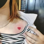 Фото минималистичной татуировки на ключице с изображением маленького красного сердца. Простой и элегантный дизайн.