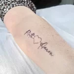 Фото тату с надписями 'Ruth' и 'Aaron', соединенными маленьким сердечком. Черно-белая татуировка на руке, выполненная в тонком, изящном стиле.