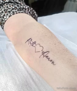 Фото тату с надписями 'Ruth' и 'Aaron', соединенными маленьким сердечком. Черно-белая татуировка на руке, выполненная в тонком, изящном стиле.