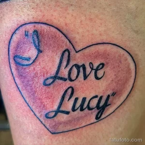 Фото тату с надписью 'Love Lucy' внутри контура сердца. Черно-красная татуировка на руке, выполненная в минималистичном стиле.