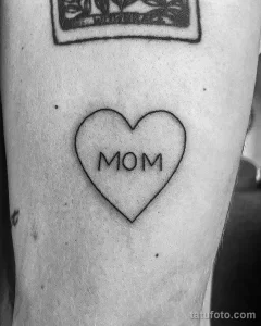 Фото тату: черное сердце с надписью "MOM" внутри, выполненное на руке. Простая и трогательная татуировка в стиле лайнарт.