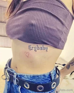 Фото тату: татуировка надписи "Crybaby" в готическом стиле с маленьким сердцем. Черно-белая татуировка на теле.