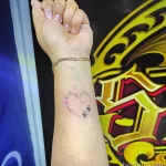 Фото тату: Небольшой рисунок котенка с розовым цветком на женском запястье, выполненный в нежных пастельных тонах.