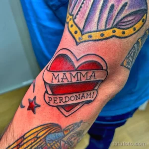 Фото тату: Красное сердце с надписью 'Mamma Perdónami' на руке, выполненное в традиционном стиле с элементами графики.