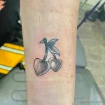 Фото тату двух спелых вишен с листьями, выполненное в стиле дотворк тонкими линиями и точками на руке.