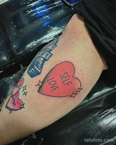 Фото тату на бедре: надпись "SELF LOVE" с сердечками и звездочками. Позитивный и вдохновляющий рисунок татуировки.