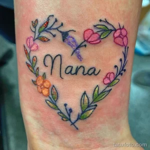 Фото тату: сердце, образованное цветами и листьями, с надписью "Nana" внутри, выполненное в ярких и нежных цветах. Расположение - на запястье.