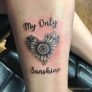 Фото тату подсолнуха, стилизованного под сердце, с надписью 'My Only Sunshine' на предплечье. Черно-белый рисунок татуировки в нежном стиле.