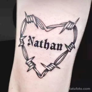Фото татуировки на руке: сердце, обвитое колючей проволокой, с именем "Nathan" внутри. Черно-белый рисунок.