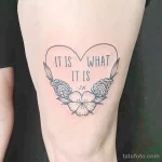 Фото тату сердца, обрамленного цветами, с надписью "IT IS WHAT IT IS" и инициалами "J.W". Эскиз татуировки выполнен в черно-белой гамме.